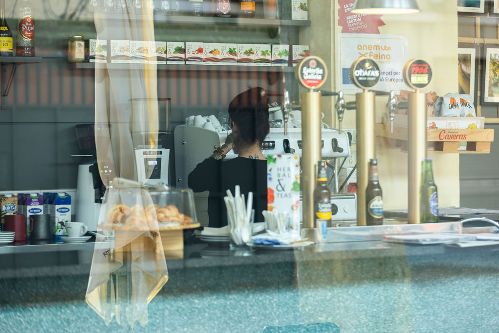 Detall d'una treballadora en formació preparant un servei a la barra de la cafeteria, simbolitzant el consum responsable i la qualitat del servei.
