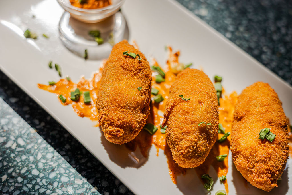 Primer pla de dues croquetes artesanes decorades amb salsa i brots sobre un plat de ceràmica, simbolitzant la cuina de KM 0 i producte del Penedès.